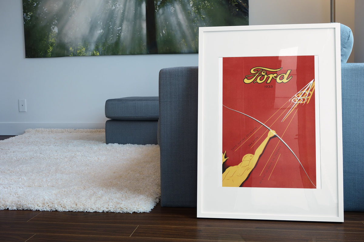 Ford V8 1933 poster in a white frame leaning beside a blue sofa