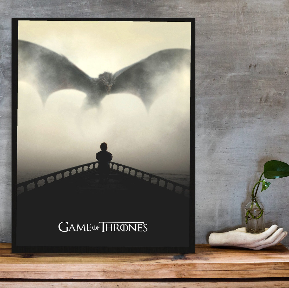 Game of Thrones Dragon Silhouette Art poster in a black frame on a wooden shelf against concrete