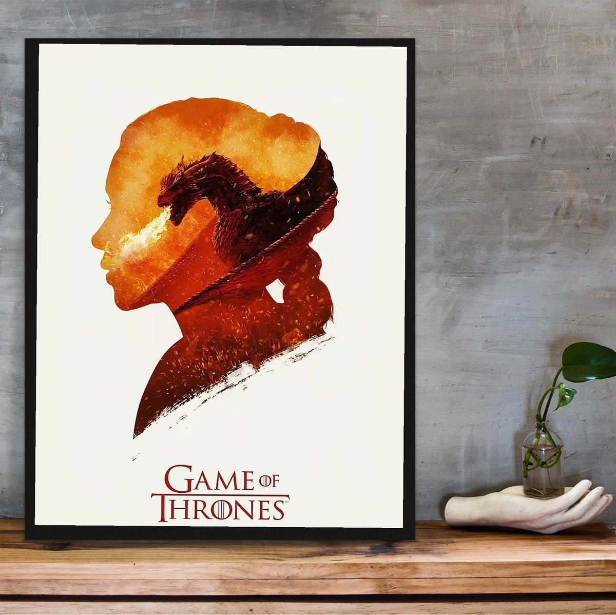Game of Thrones Silhouette Art poster in a black frame on a wooden shelf against concrete