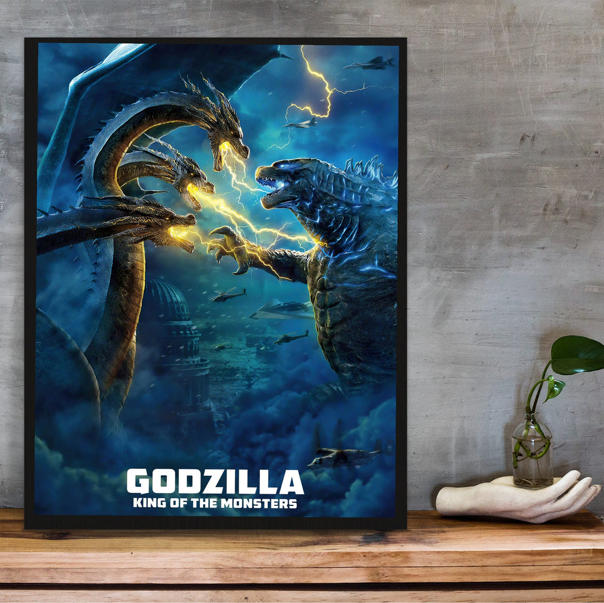 Godzilla: King of the Monsters (2019) Movie Ghidorah Battle Art poster in a black frame on a wooden shelf against concrete