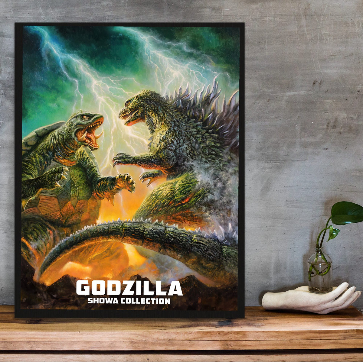 Godzilla Showa Era Movie Collection Art poster in a black frame on a wooden shelf against concrete