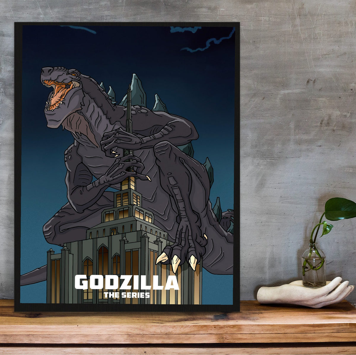 Godzilla: The Series Key Art poster in a black frame on a wooden shelf against concrete