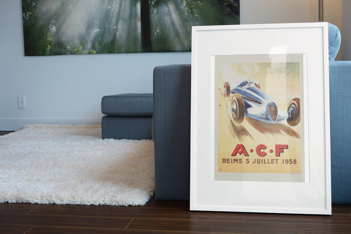 Grand Prix de l'ACF Reims 1938 poster in a white frame leaning beside a blue sofa