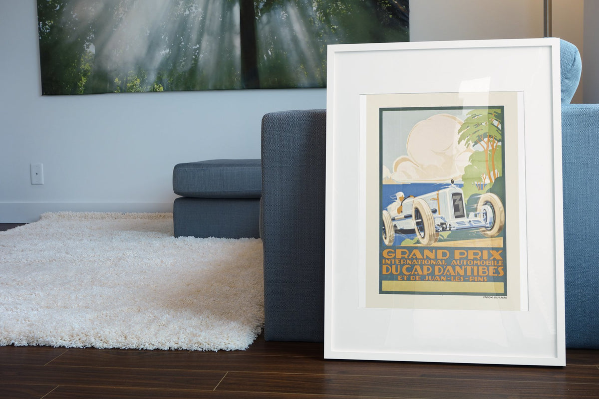 Grand Prix du Cap d'Antibes et de Juan-les-Pins poster in a white frame leaning beside a blue sofa