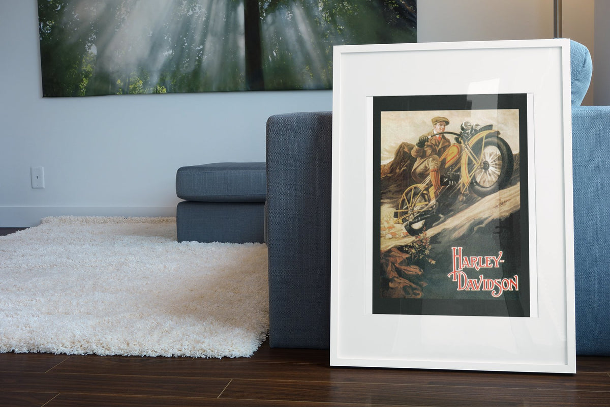 Harley-Davidson 1920s poster in a white frame leaning beside a blue sofa