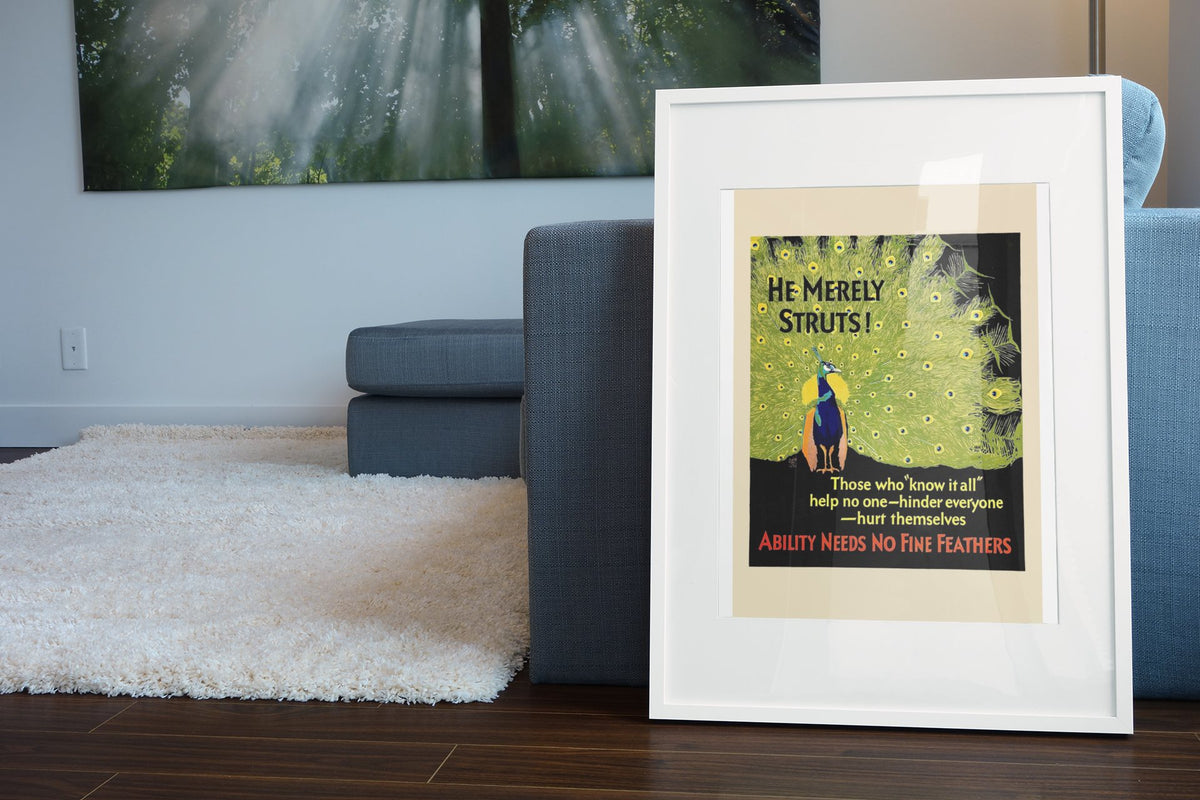 He Merely Struts poster in a white frame leaning beside a blue sofa
