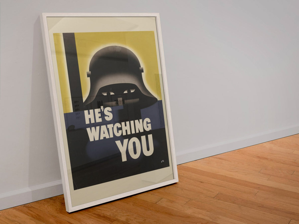 Hes Watching You poster in a white frame leaning against a wall