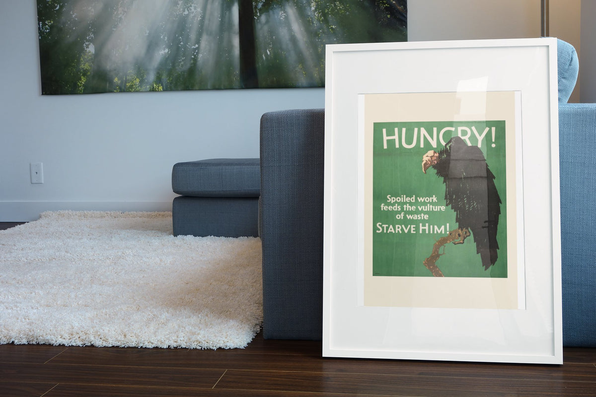 Hungry poster in a white frame leaning beside a blue sofa