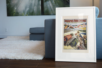 Indianapolis Motor Speedway poster in a white frame leaning beside a blue sofa
