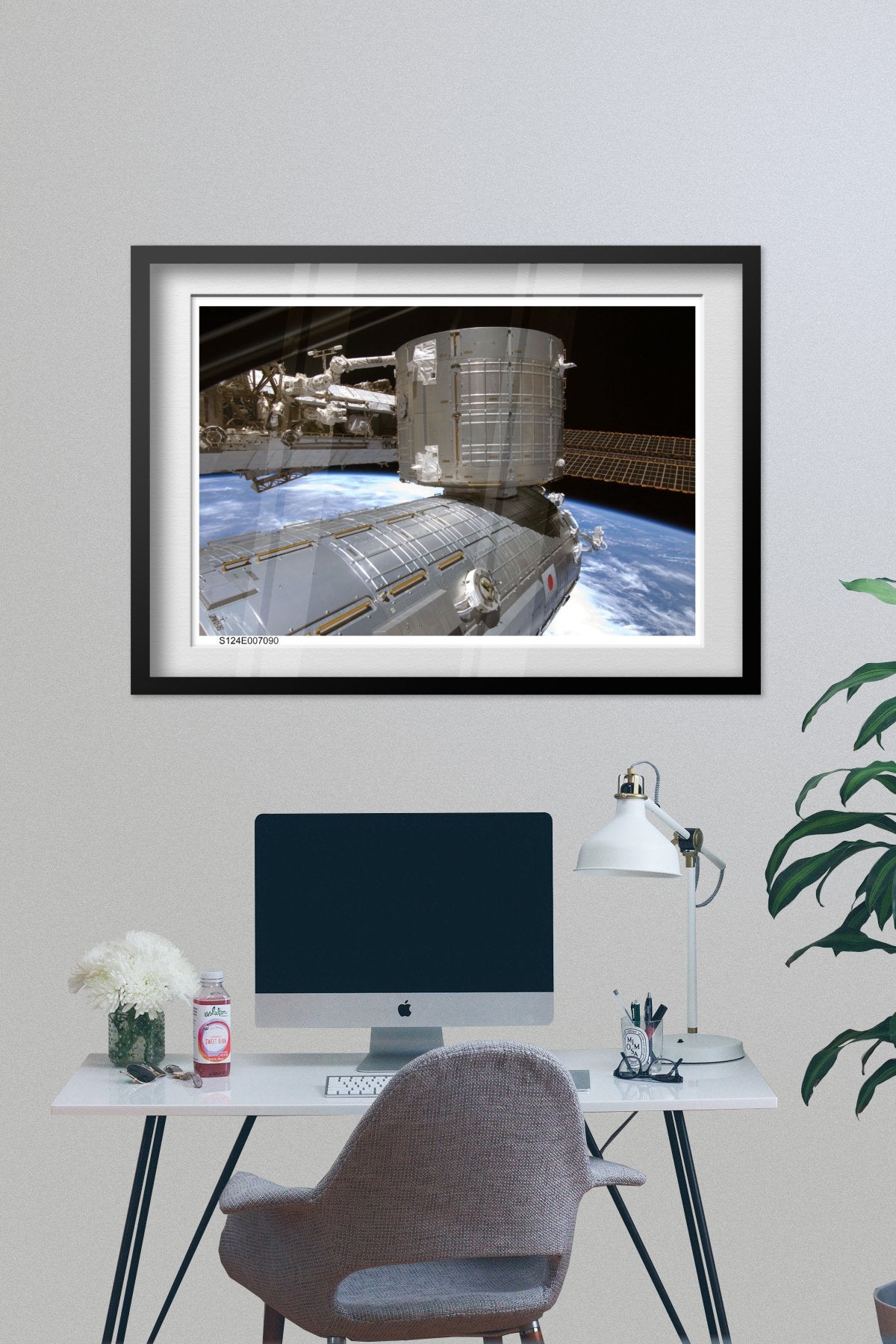 International Space Station over Earth poster framed above a desk with a computer