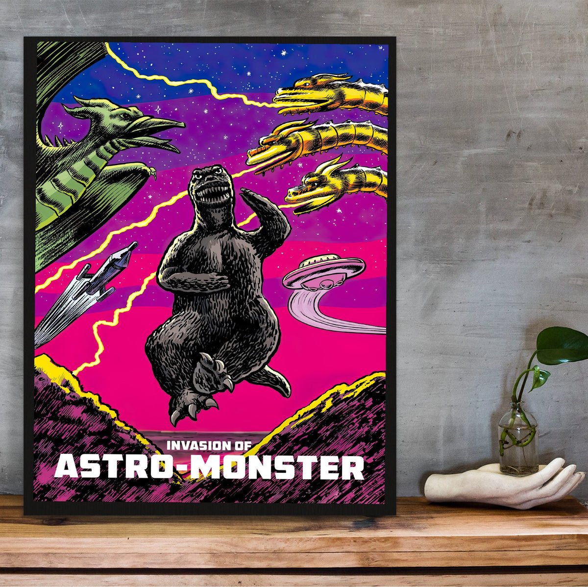 Invasion of Astro-Monster (1965) Movie Illustrated Art poster in a black frame on a wooden shelf against concrete