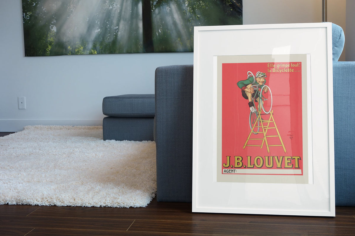JB Louvet Bicycle on a Ladder poster leaning beside a blue sofa
