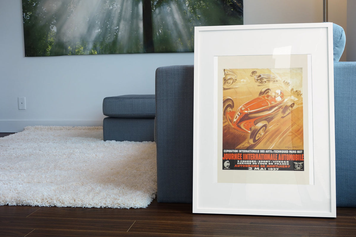Journée Internationale Automobile Paris 1937 poster in a white frame leaning beside a blue sofa