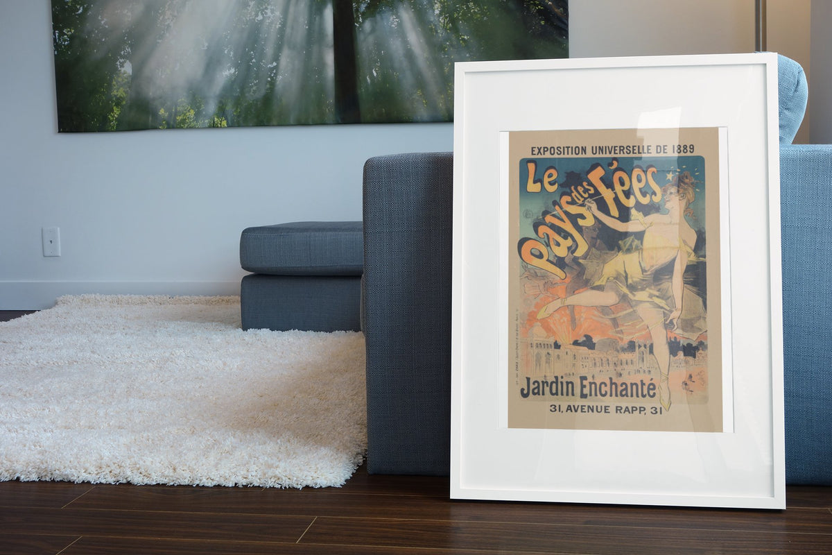 Jules Chéret Le Pays des Fées poster in a white frame leaning beside a blue sofa