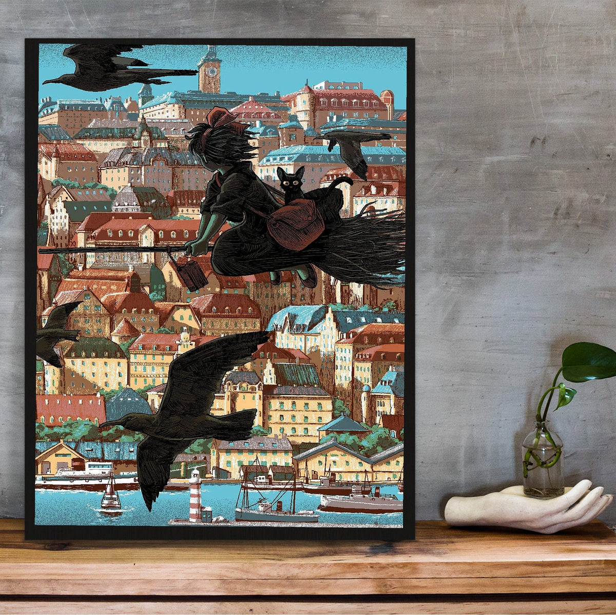 Kiki's Delivery Service Koriko Town Illustrated Art poster in a black frame on a wooden shelf against concrete