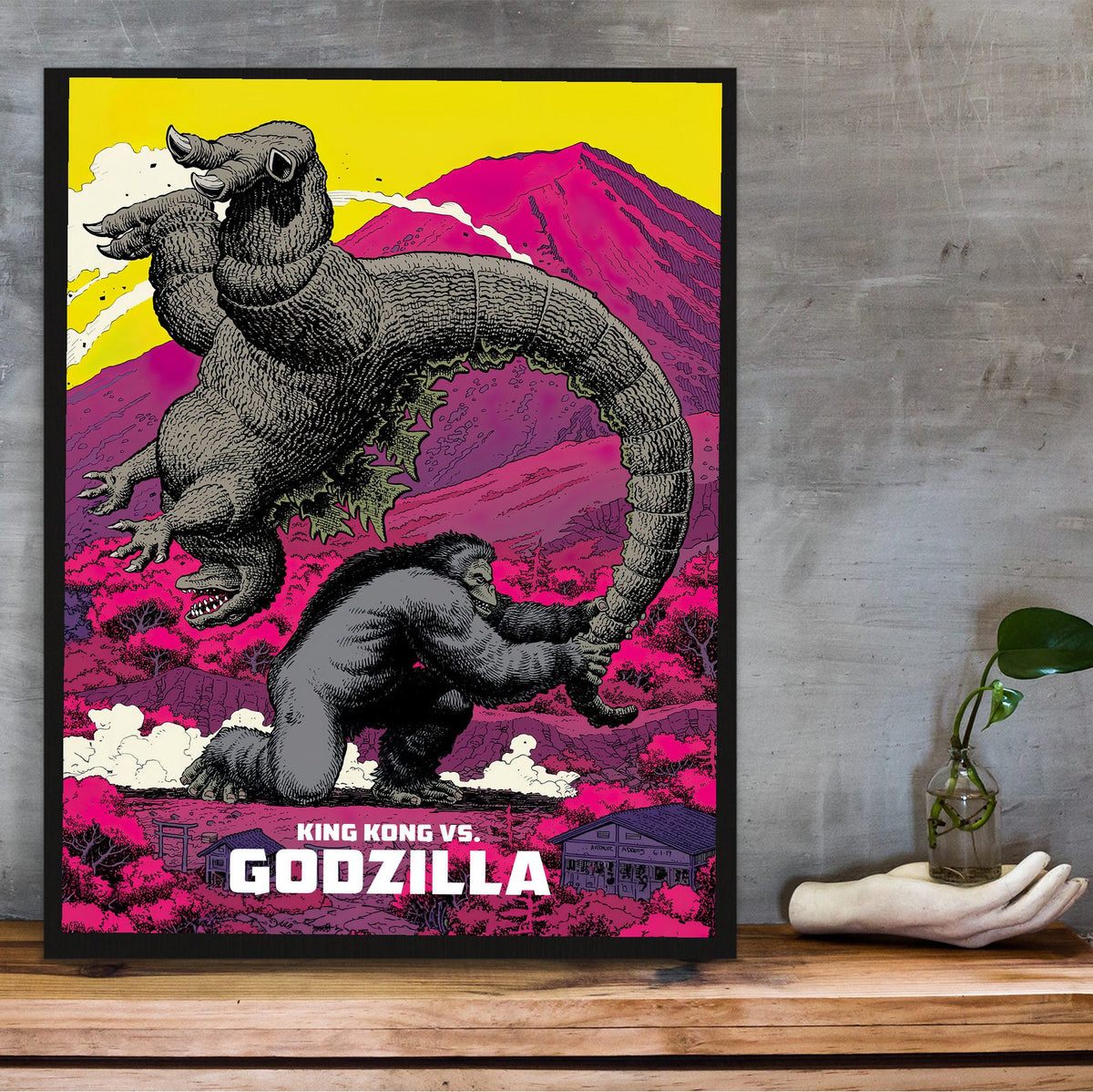 King Kong vs. Godzilla (1962) Movie Pop Art poster in a black frame on a wooden shelf against concrete