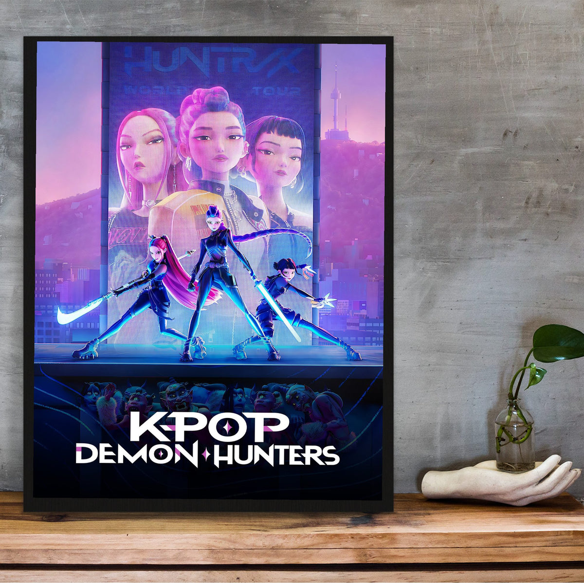 KPop Demon Hunters (2025) Movie Huntrix Key Art poster in a black frame on a wooden shelf against concrete