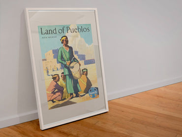 Land of Pueblos Santa Fe poster in a white frame leaning against a wall