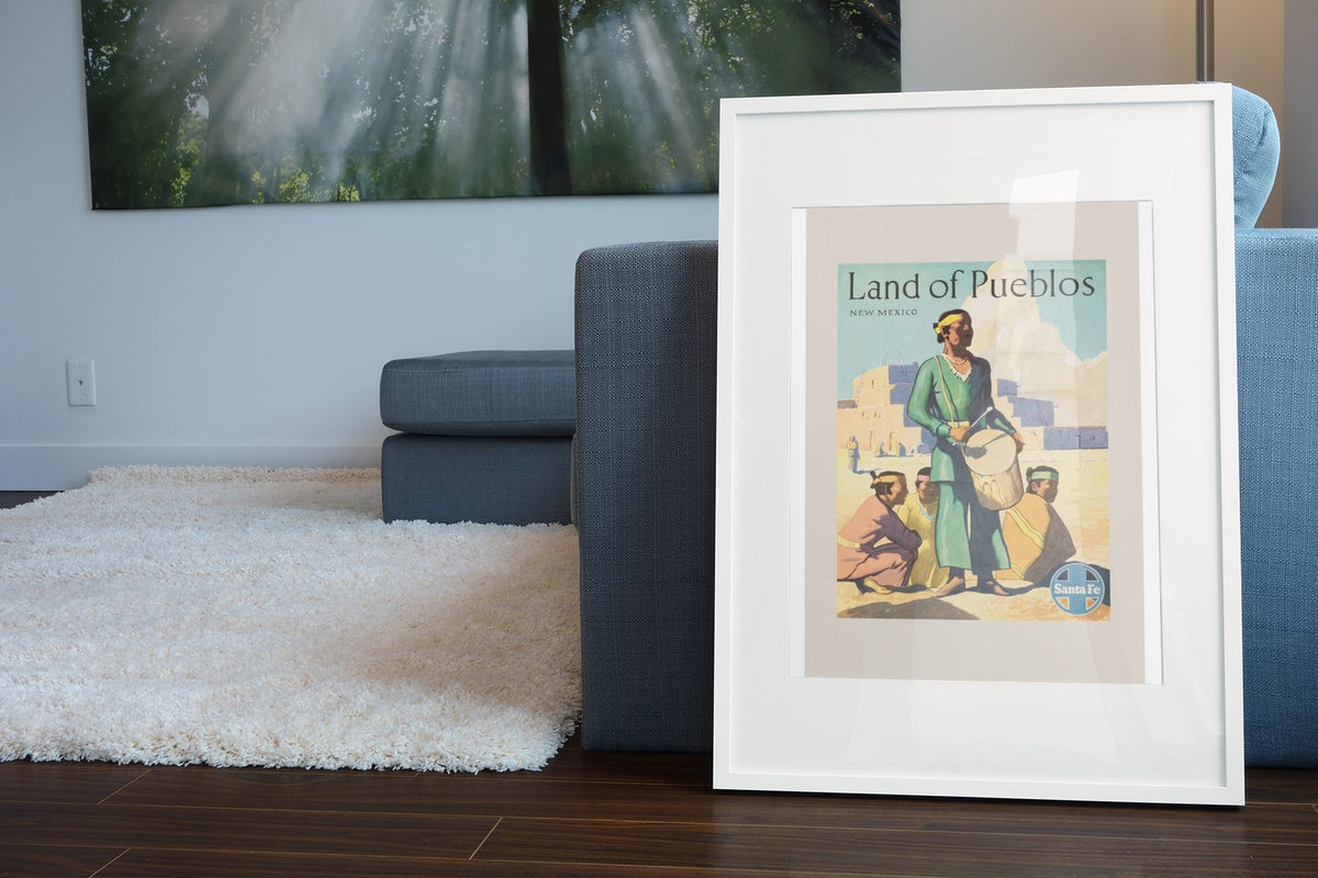 Land of Pueblos Santa Fe poster leaning beside a blue sofa
