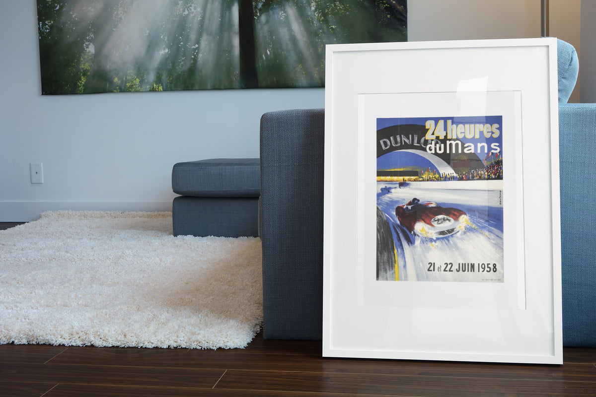 24 Heures du Mans 1958 poster in a white frame leaning beside a blue sofa
