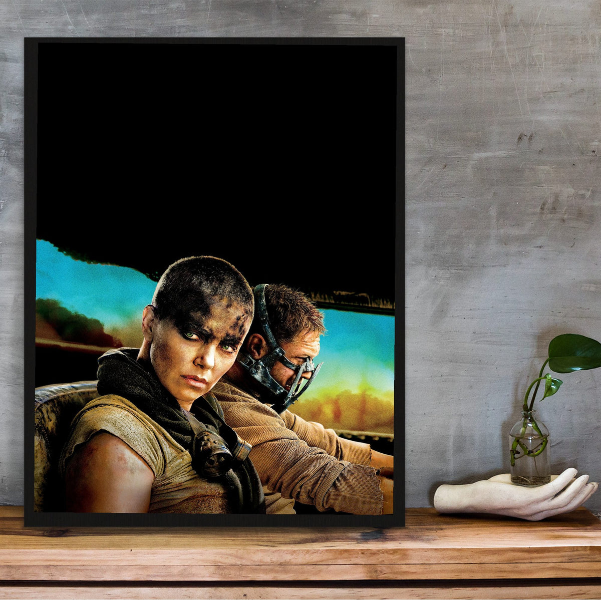 Mad Max: Fury Road (2015) Movie Furiosa and Max Portrait Art poster in a black frame on a wooden shelf against concrete