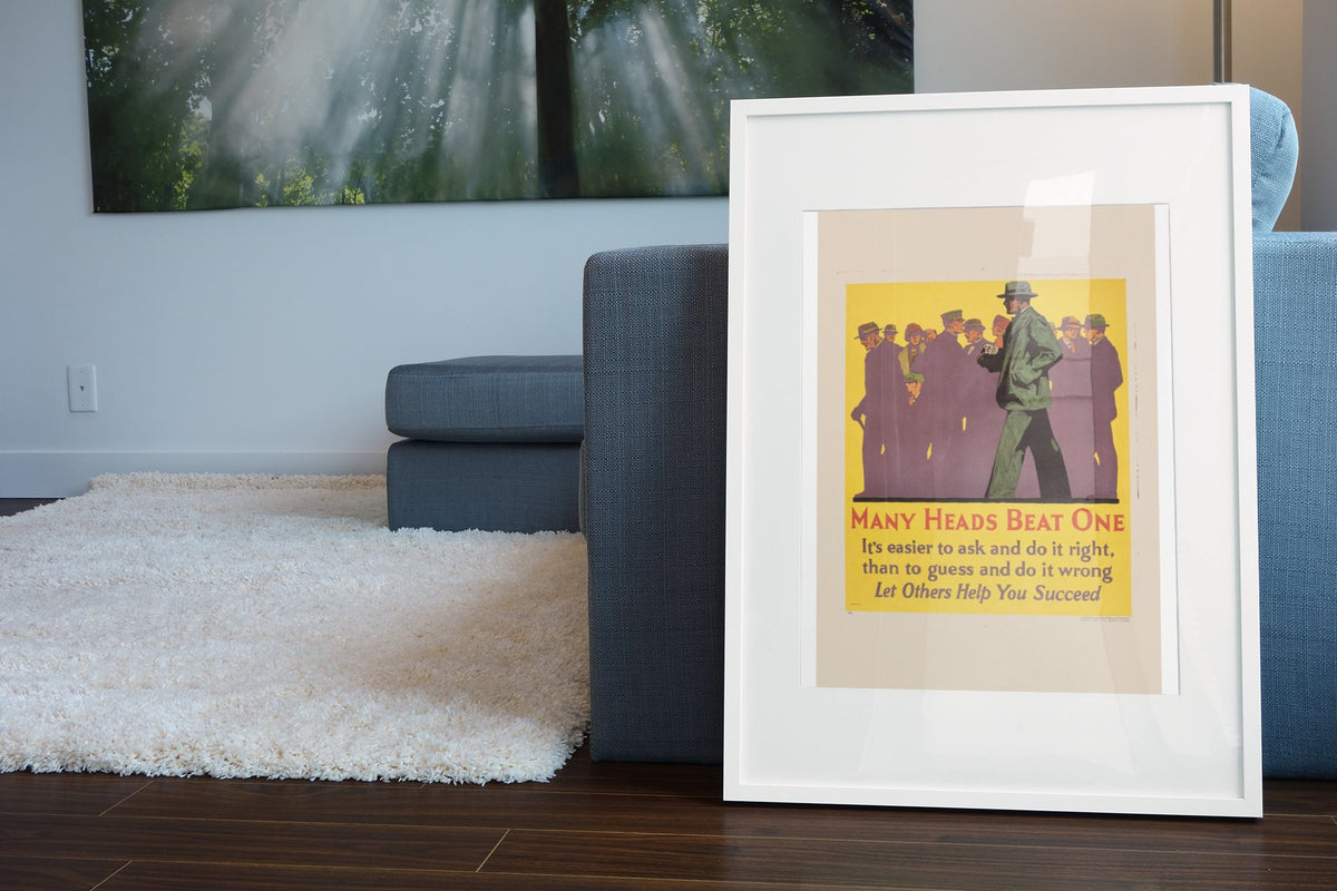 Many Heads Beat One poster in a white frame leaning beside a blue sofa