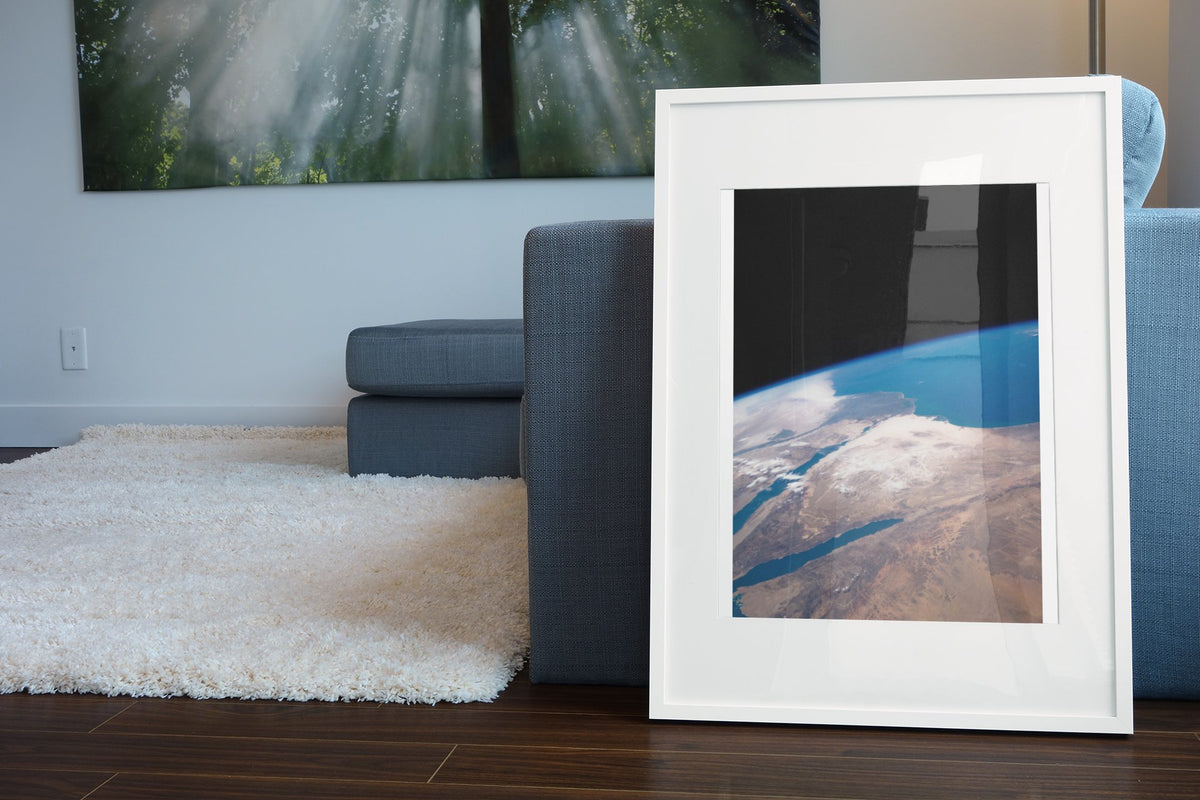 The Middle East seen from space poster in a white frame leaning beside a blue sofa
