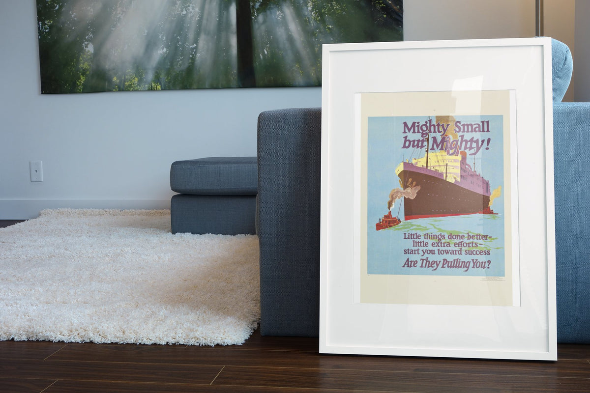 Mighty Small but Mighty poster in a white frame leaning beside a blue sofa