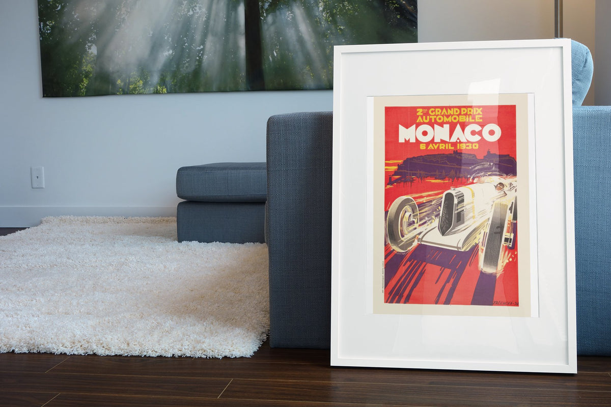 Monaco Grand Prix 1930 poster in a white frame leaning beside a blue sofa