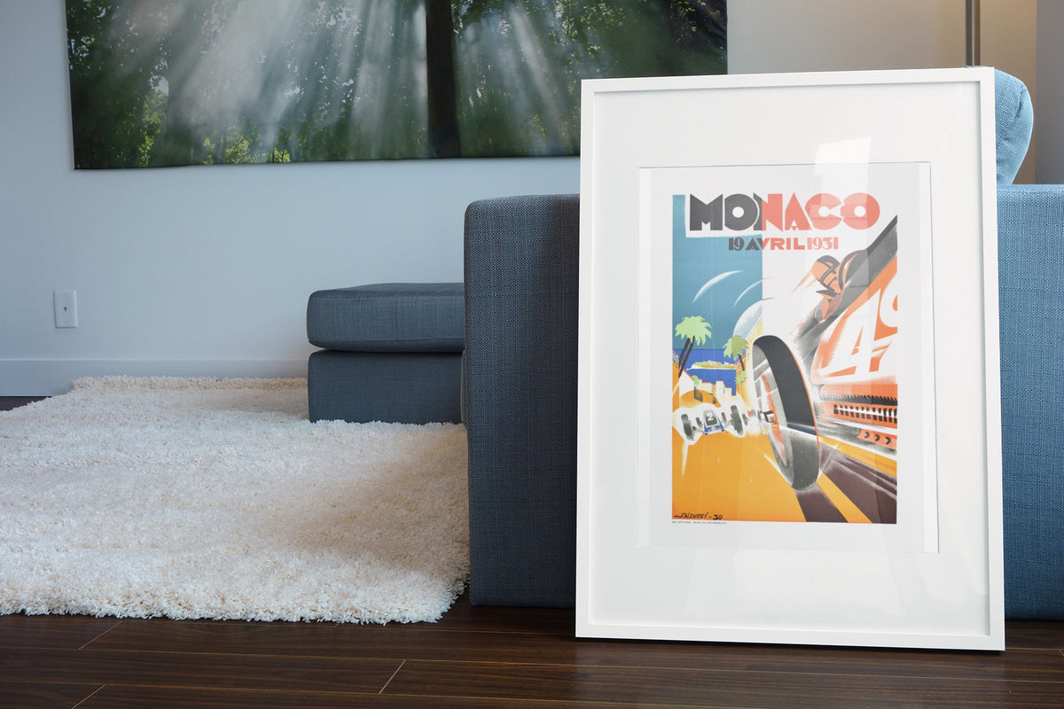 Monaco Grand Prix 1931 poster in a white frame leaning beside a blue sofa