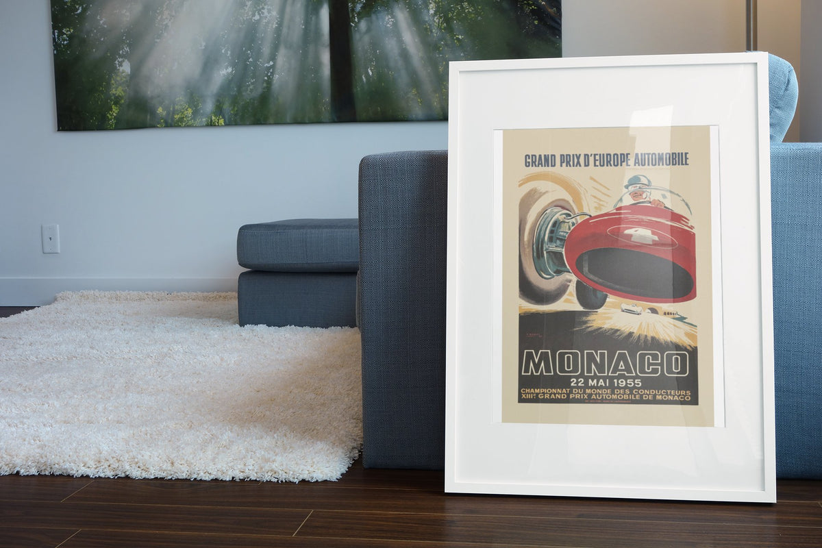 Monaco Grand Prix 1955 poster in a white frame leaning beside a blue sofa