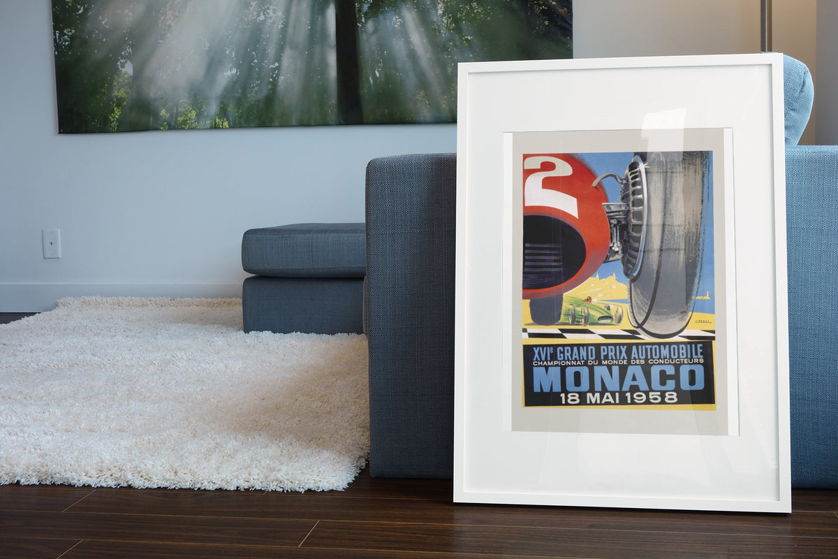 Monaco Grand Prix 1958 poster in a white frame leaning beside a blue sofa