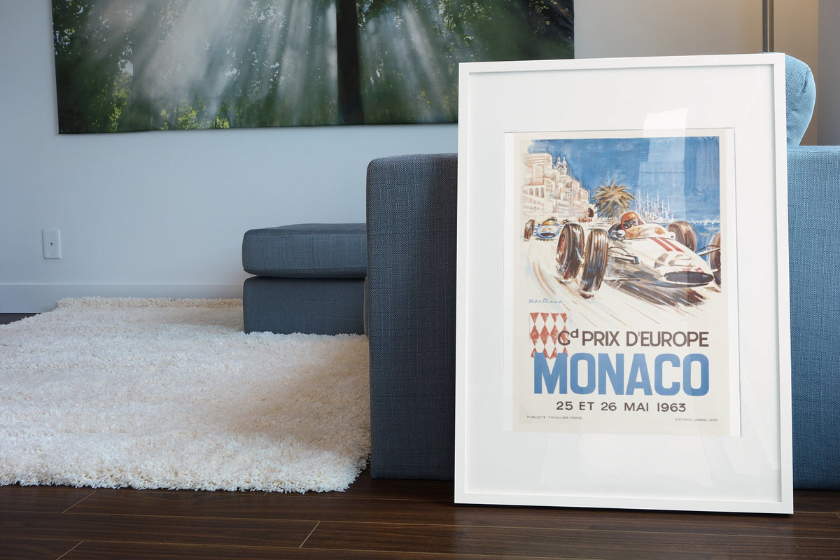Monaco Grand Prix 1963 poster in a white frame leaning beside a blue sofa