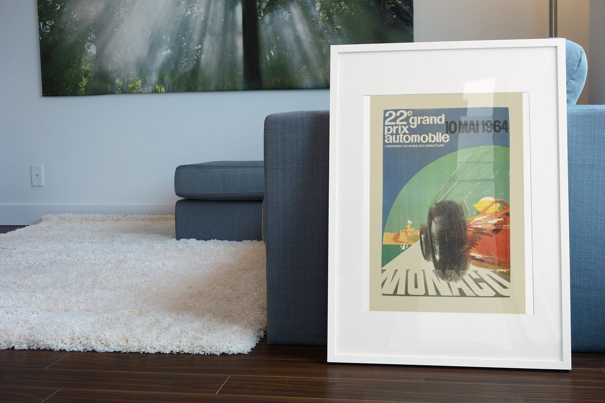 Monaco Grand Prix 1964 poster in a white frame leaning beside a blue sofa
