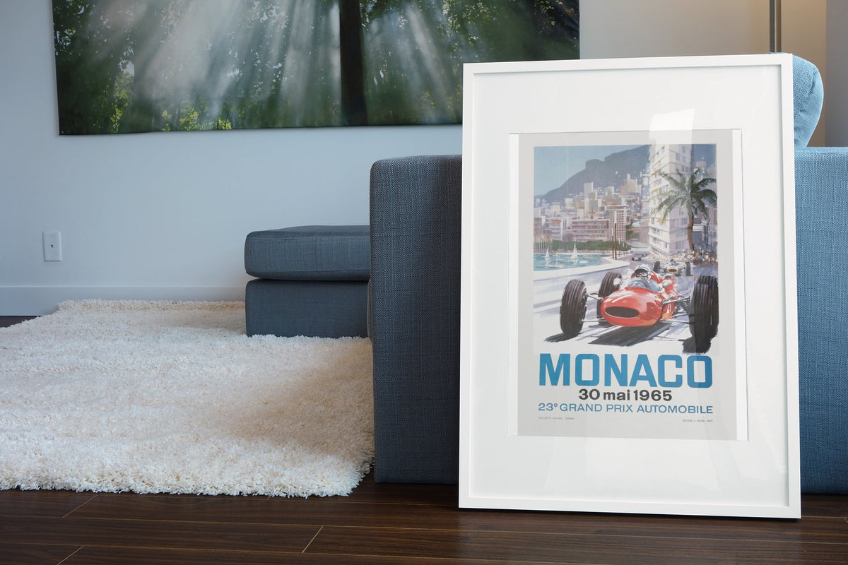 Monaco Grand Prix 1965 poster in a white frame leaning beside a blue sofa