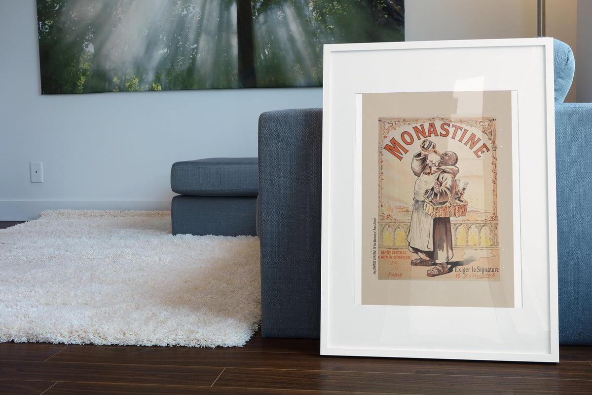Monastine 1892 French liqueur poster in a white frame leaning beside a blue sofa