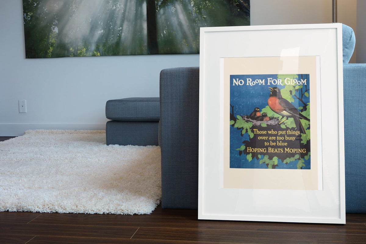 No Room for Gloom poster in a white frame leaning beside a blue sofa