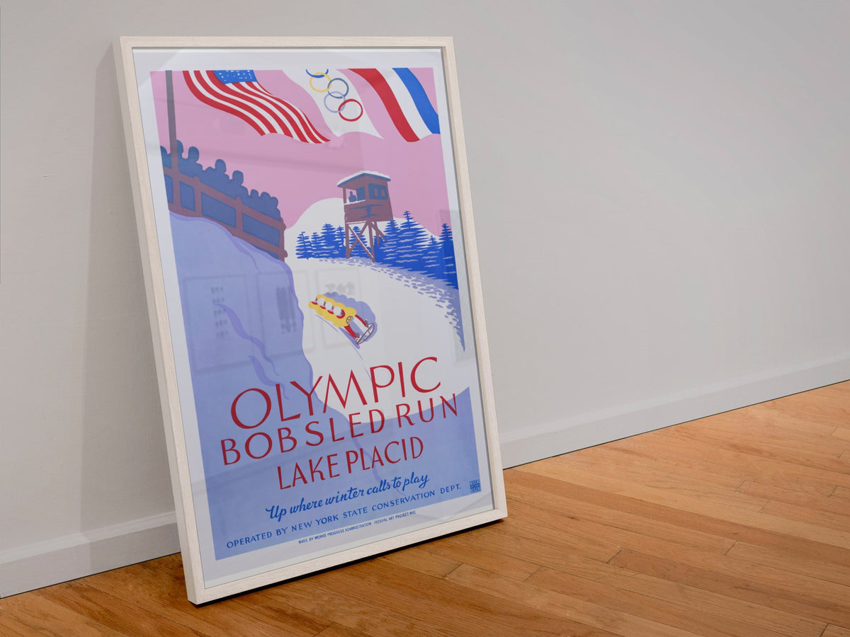 Olympic Bobsled Run Lake Placid 1938 poster in a white frame leaning against a wall