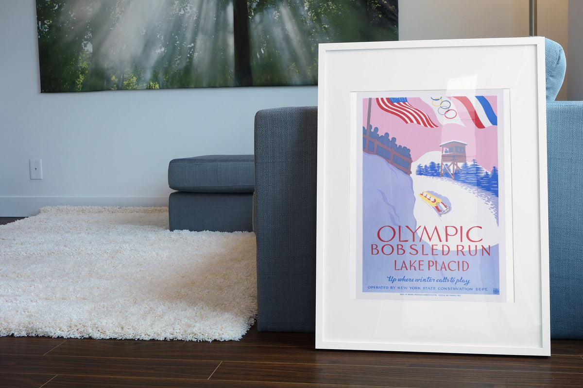 Olympic Bobsled Run Lake Placid 1938 poster leaning beside a blue sofa