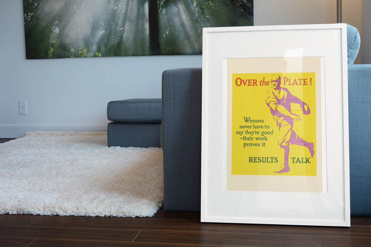 Over the Plate poster in a white frame leaning beside a blue sofa