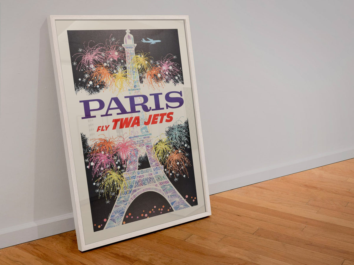 Paris Fly TWA Jets Fireworks poster in a white frame leaning against a wall
