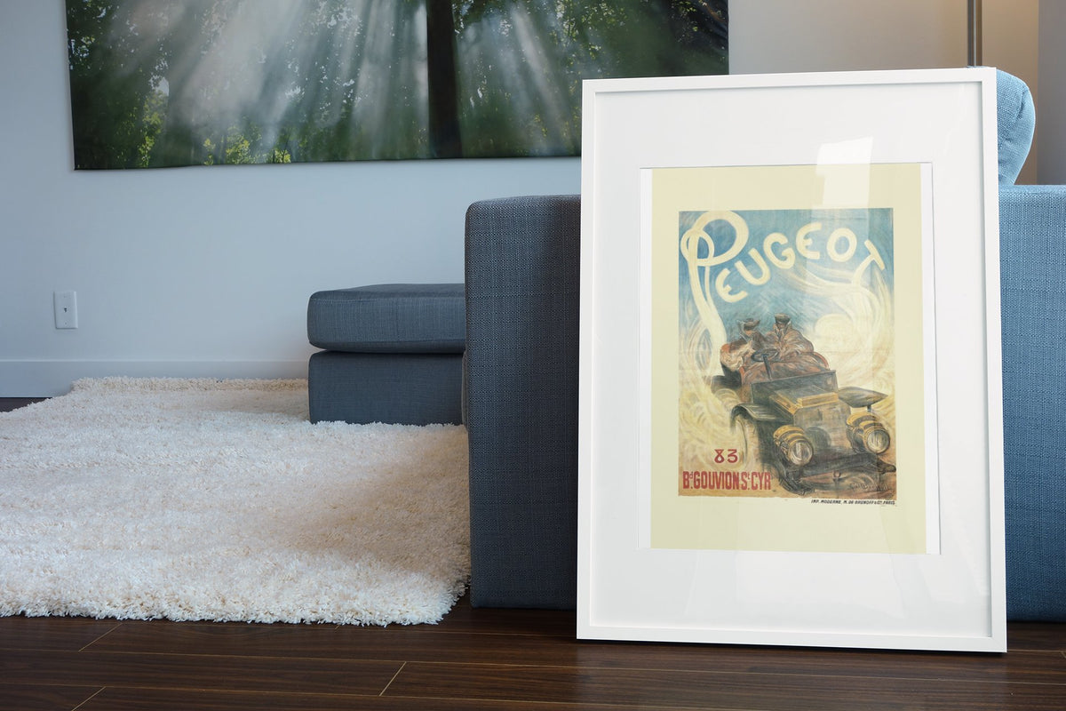 Peugeot poster in a white frame leaning beside a blue sofa