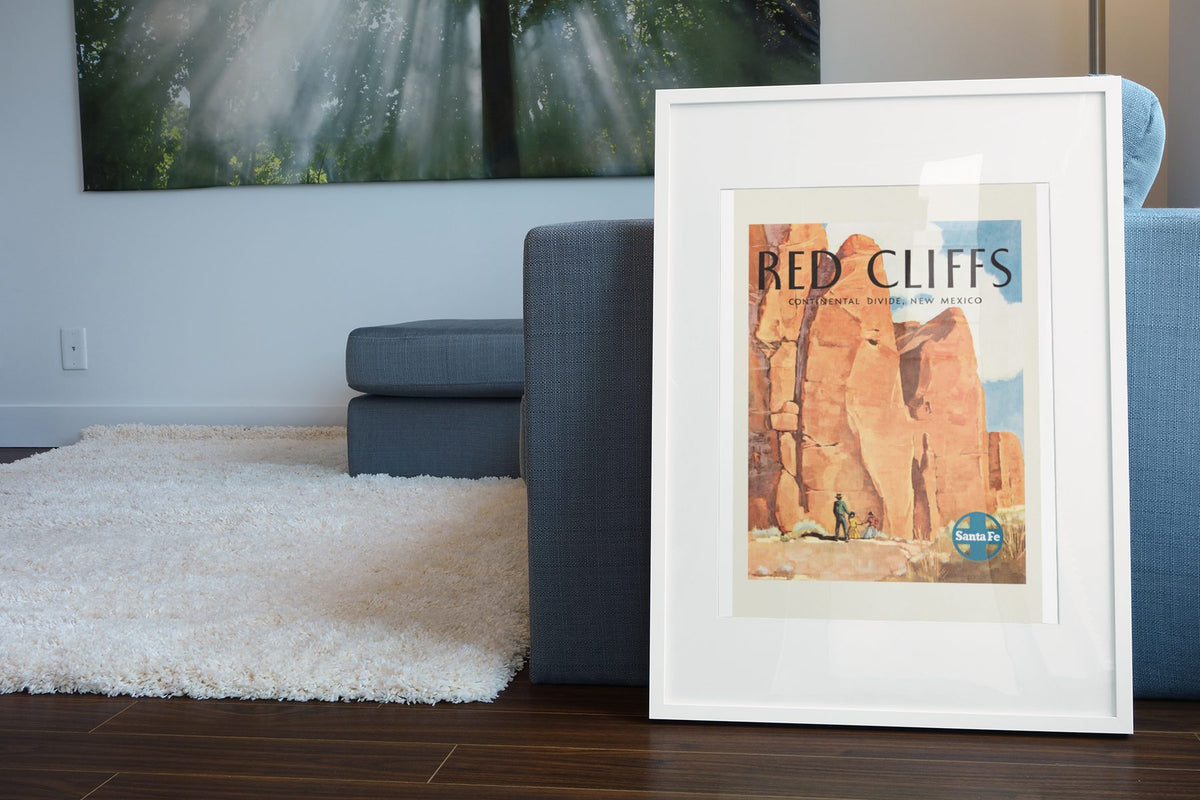 Red Cliffs New Mexico Santa Fe poster leaning beside a blue sofa