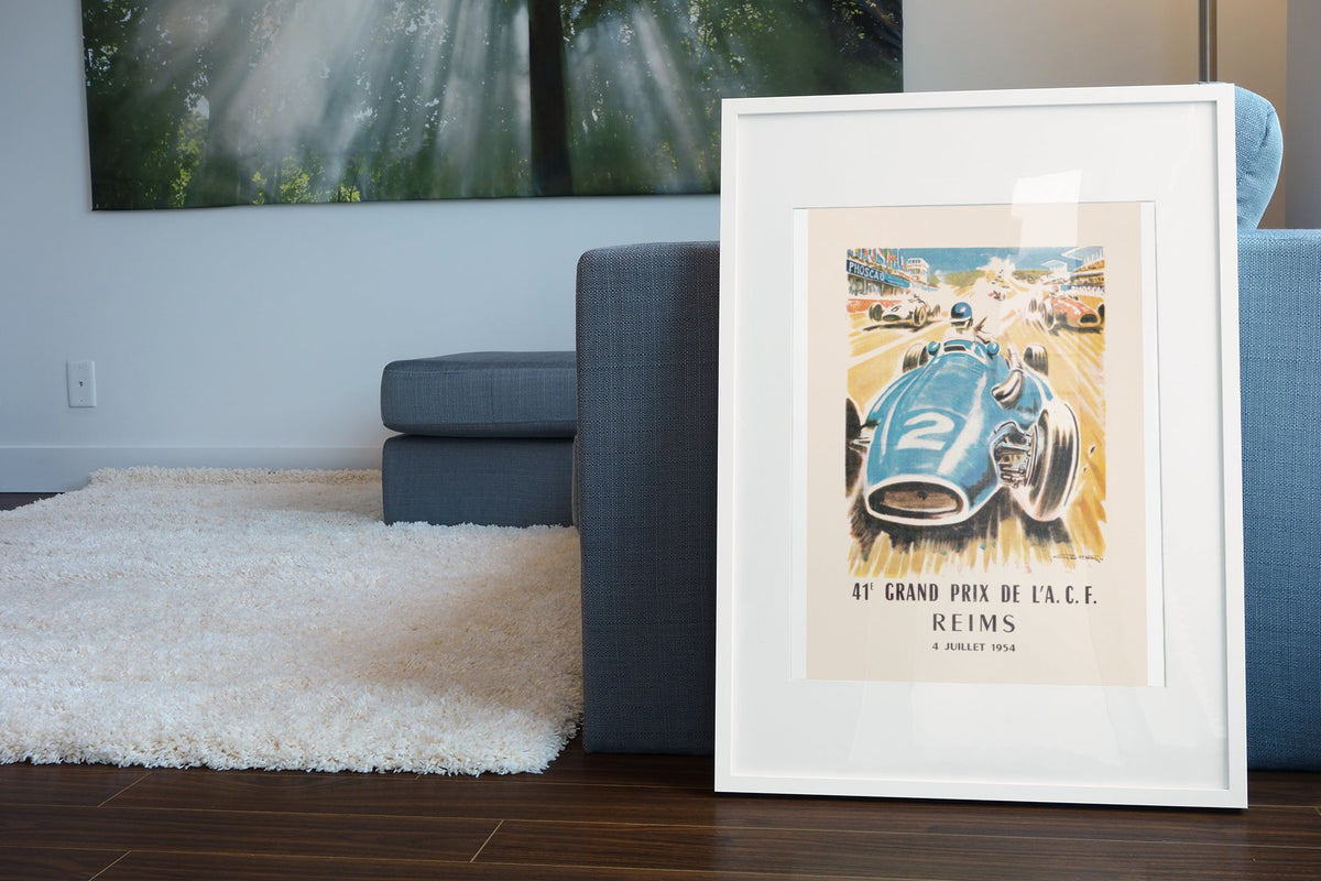 Grand Prix de l'ACF Reims 1954 poster in a white frame leaning beside a blue sofa