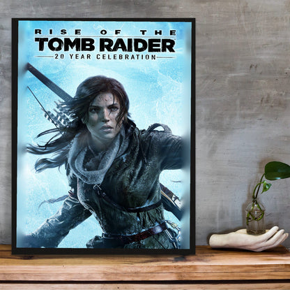 Rise of the Tomb Raider 20 Year Celebration Art poster in a black frame on a wooden shelf against concrete