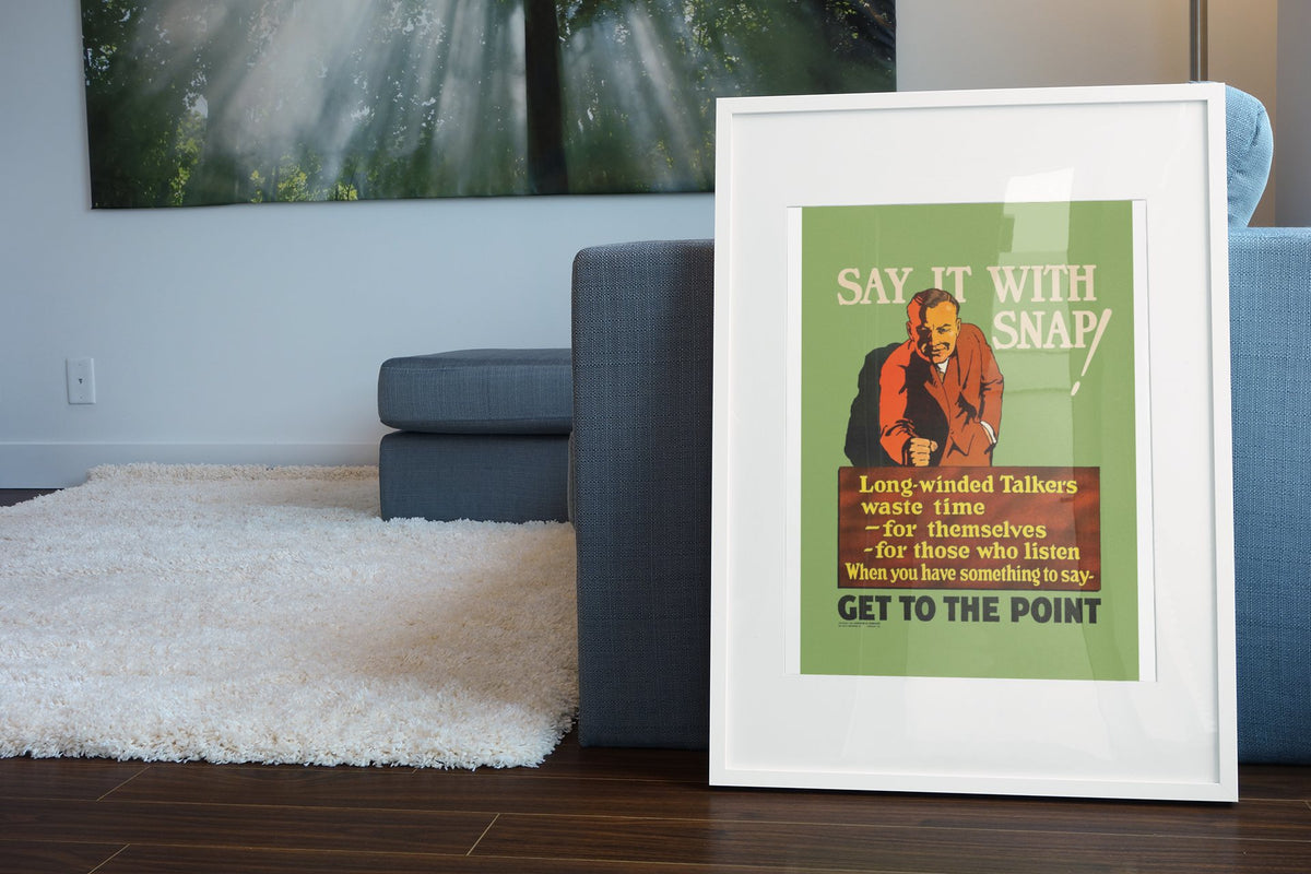 Say It With Snap poster in a white frame leaning beside a blue sofa