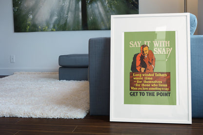 Say It With Snap poster in a white frame leaning beside a blue sofa