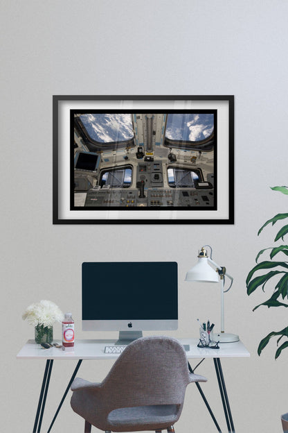 Space Shuttle Atlantis cockpit poster framed above a desk with a computer