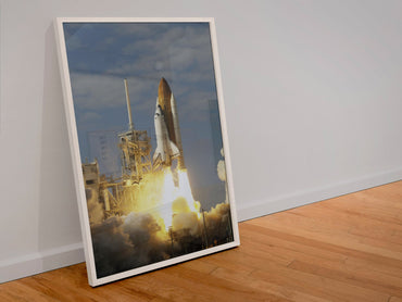 Space Shuttle Atlantis STS-122 launch poster in a white frame leaning against a wall