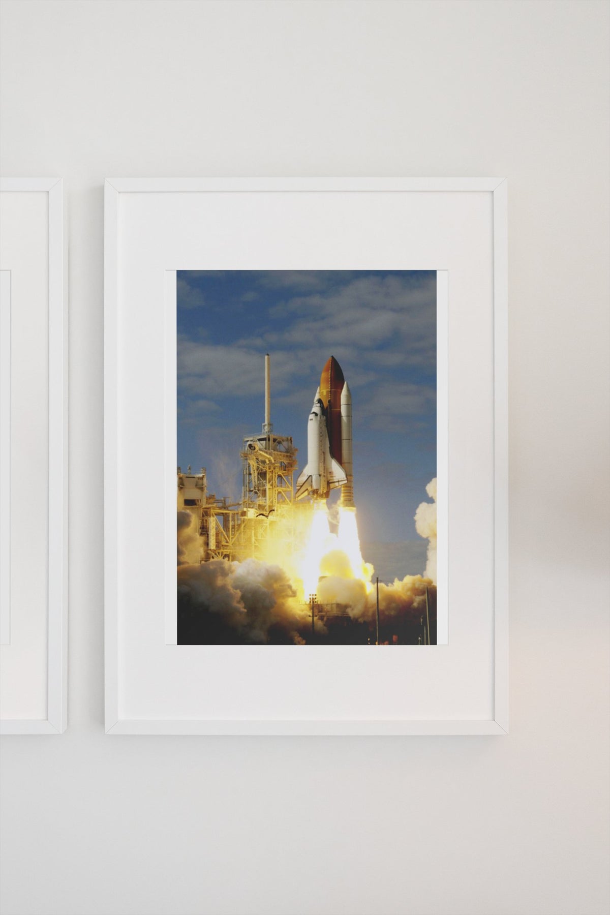 Space Shuttle Atlantis STS-122 launch poster in a white frame on a light wall